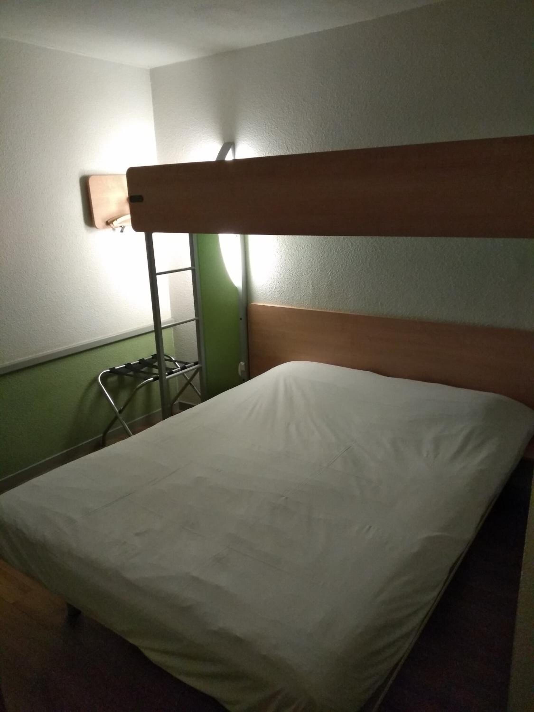 A single bed with a wooden headboard in a room with green walls and a white ceiling.