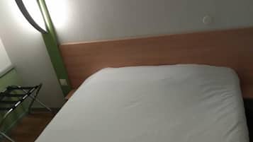 Habitación de hotel con cama, una obra de arte en la pared que representa pasto, cabecero de madera y una lámpara verde.