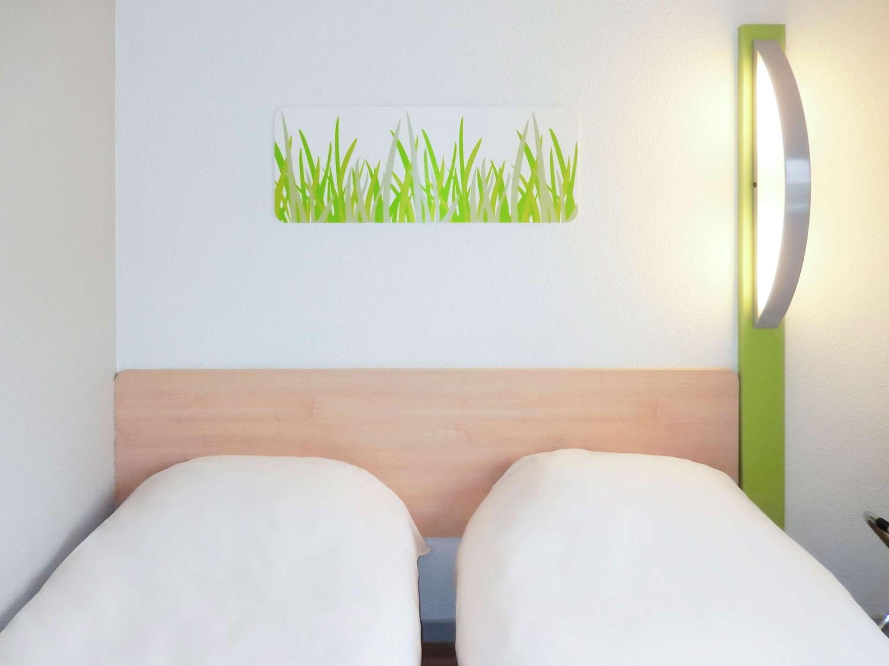 Una habitación de hotel con una cama, una lámpara de pared y un adhesivo mural con diseño de hierba.