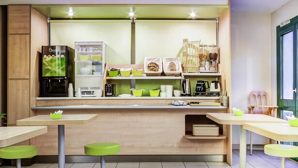 Cocina moderna con refrigerador, cafetera y diversos electrodomésticos. Hay taburetes verdes y una encimera con un lavamanos.