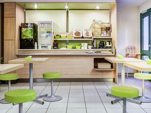 Cocina moderna con refrigerador, cafetera y diversos electrodomésticos. Hay taburetes verdes y una encimera con un lavamanos.