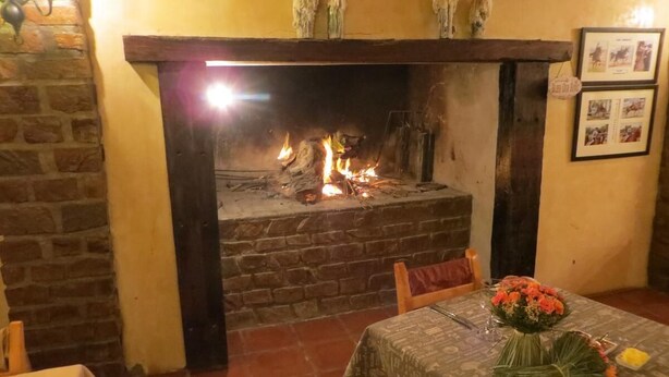Une pièce avec une cheminée en briques, une table à manger recouverte d’une nappe et un bouquet de fleurs.