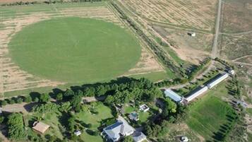 An aerial view of a residential area with a large green field, a long building with a white roof, and several smaller structures.