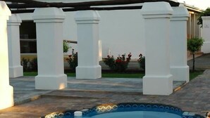 Une piscine dont le bord est revêtu de carreaux, entourée de colonnes blanches et dotée d’un patio couvert.