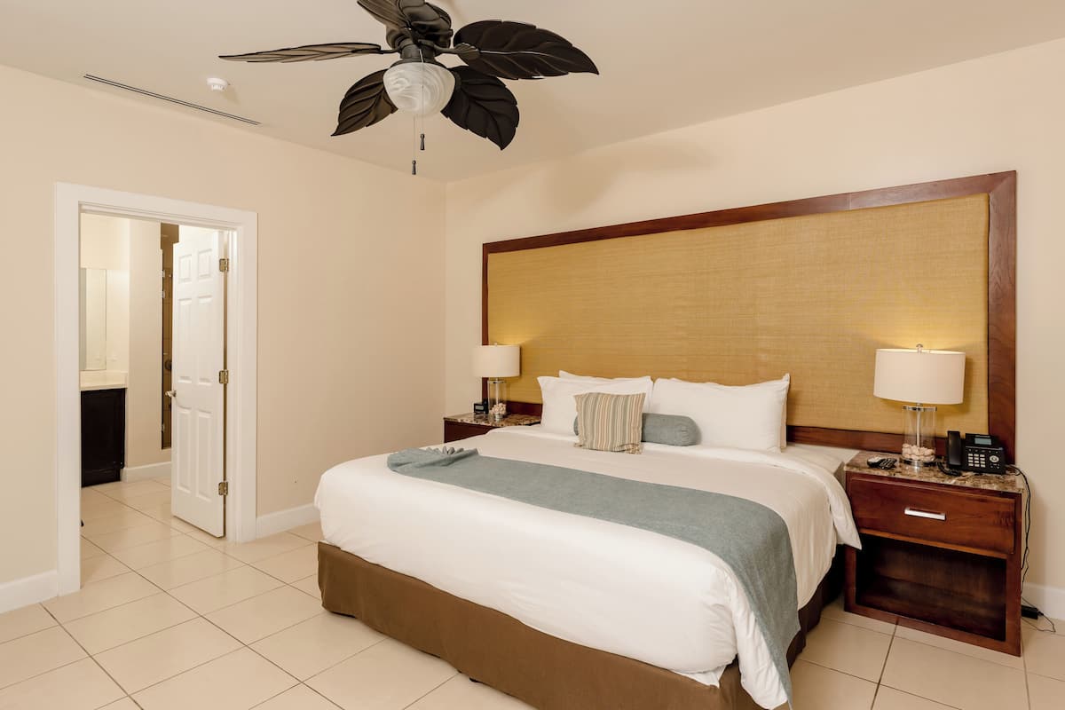 A hotel room with a large bed, two bedside tables with lamps, a ceiling fan, and a wooden headboard.