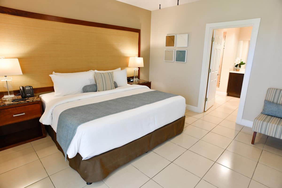 A hotel room with a large bed, two bedside tables with lamps, a chair, and a door leading to a bathroom.