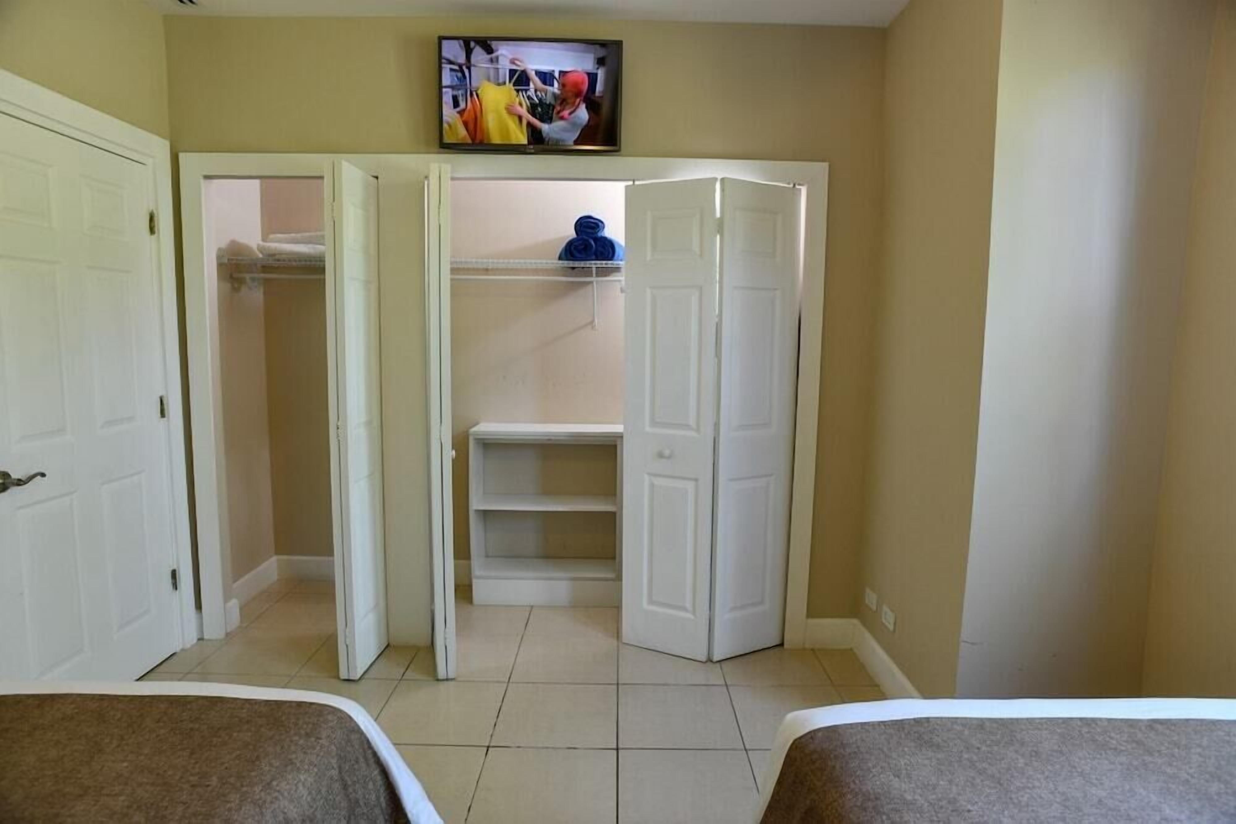 Ein Zimmer mit zwei Betten, einem geöffneten Kleiderschrank und einem an der Wand befestigten Fernseher.