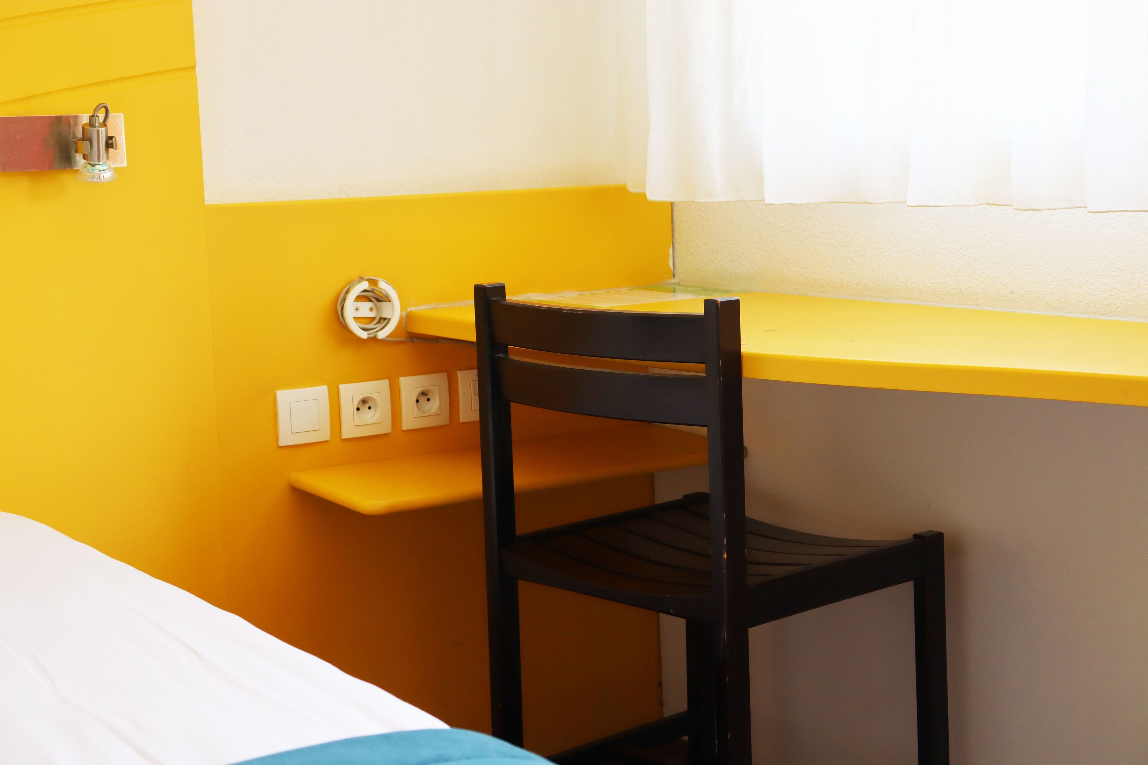 Een kamer met een bed, een bureau met stoel en een raam met gordijnen.