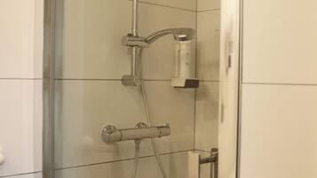 Een douchecabine met glazen wanden, een handdouche en een vastgeplaatste kraan.