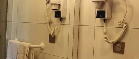 A bathroom with a sink, two hair dryers mounted on the wall, and a towel rack with a towel.
