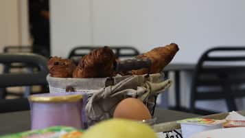 A table with a basket containing croissants, a can of yogurt, and a plate with a cup.