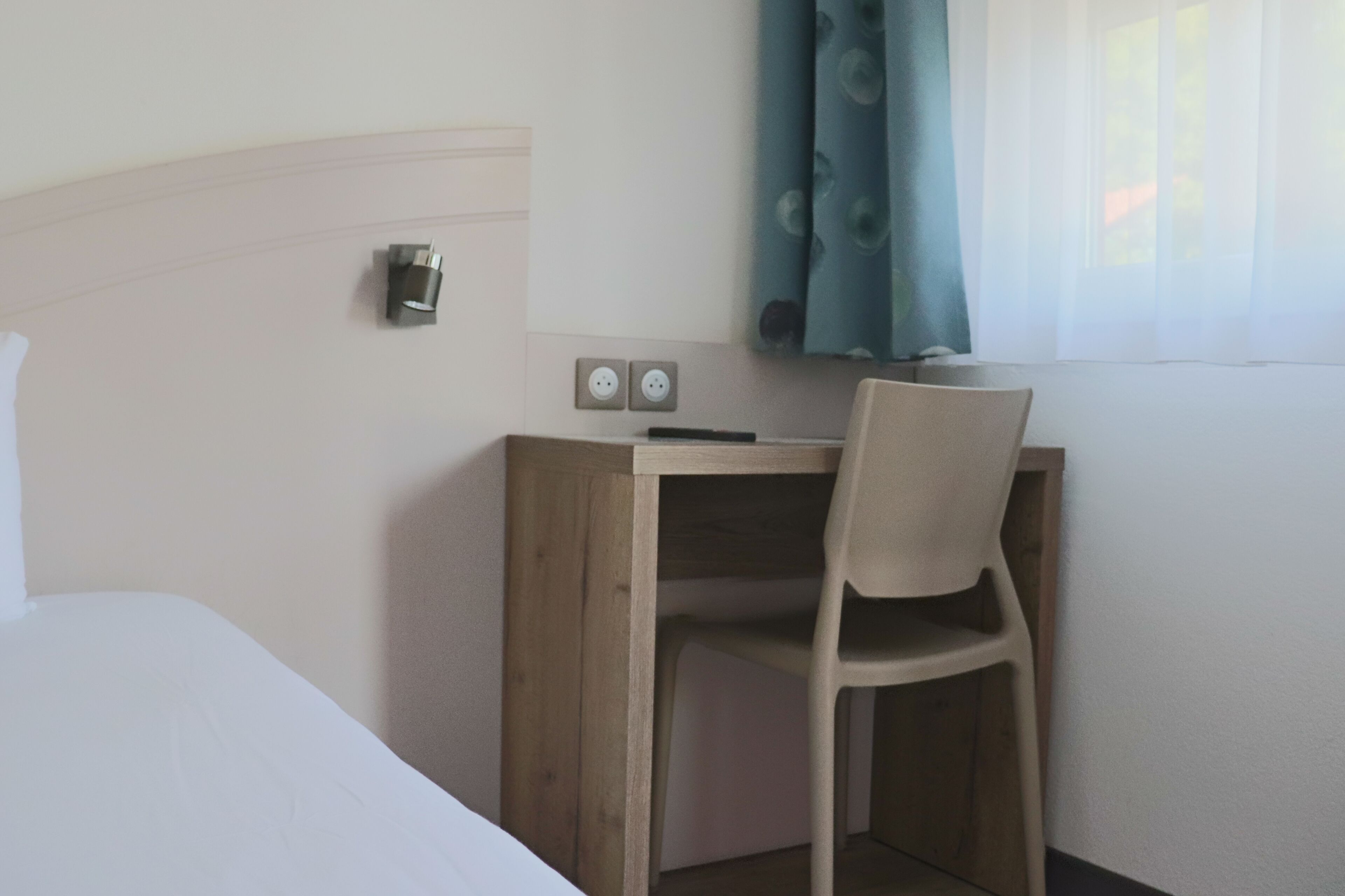 Une chambre d’hôtel avec un bureau en bois, une chaise, un lit et une fenêtre avec des rideaux.