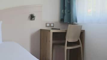 Habitación de hotel con escritorio de madera, una silla, una cama y una ventana con cortinas.