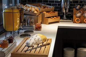 A breakfast buffet with various food items, including bread, pastries, and a large loaf of bread on a cutting board.