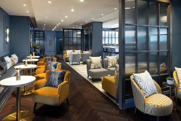 A modern lounge area with sofas and armchairs, a bar, and a large window with a view.