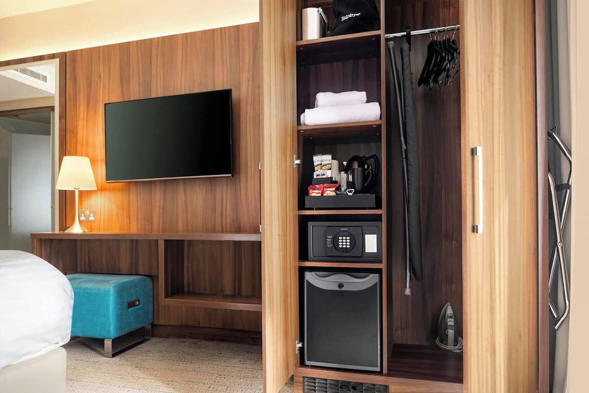 A hotel room with a flat-screen TV, a minibar, a coffee maker, and a shower area.