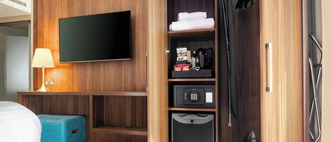 A hotel room with a flat-screen TV, a minibar, a coffee maker, and a shower area.