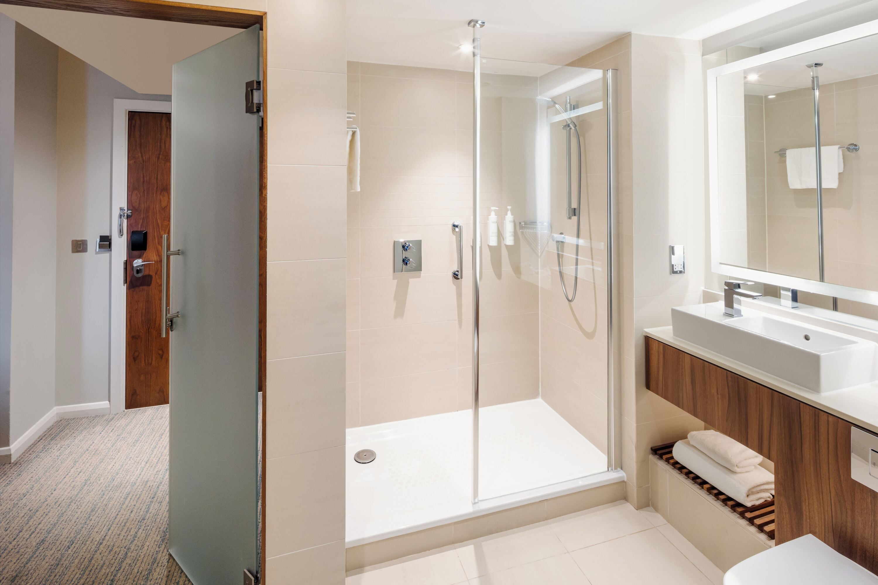 Un bany modern amb dutxa amb envà de vidre, un lavabo amb mirall i un armari de tocador de fusta.