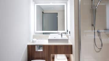 Un baño moderno con ducha envuelta en vidrio, un espejo grande y un tocador de madera con lavabo.