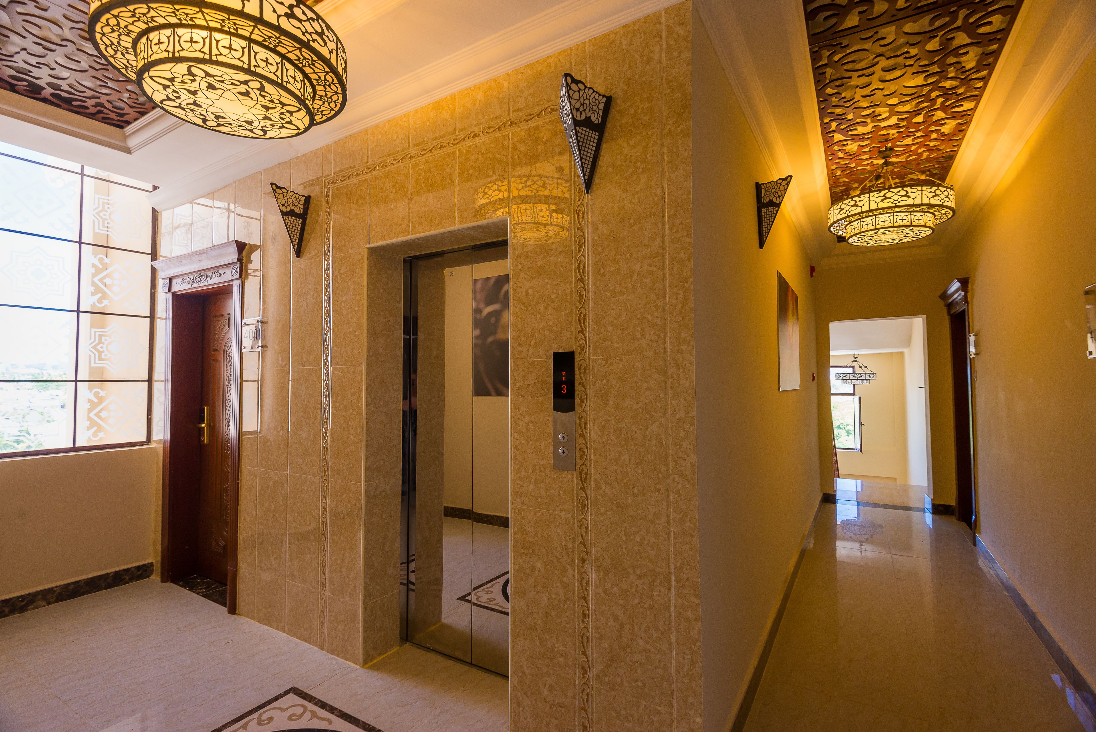 An interior hallway with an elevator, patterned walls, and decorative lighting fixtures.