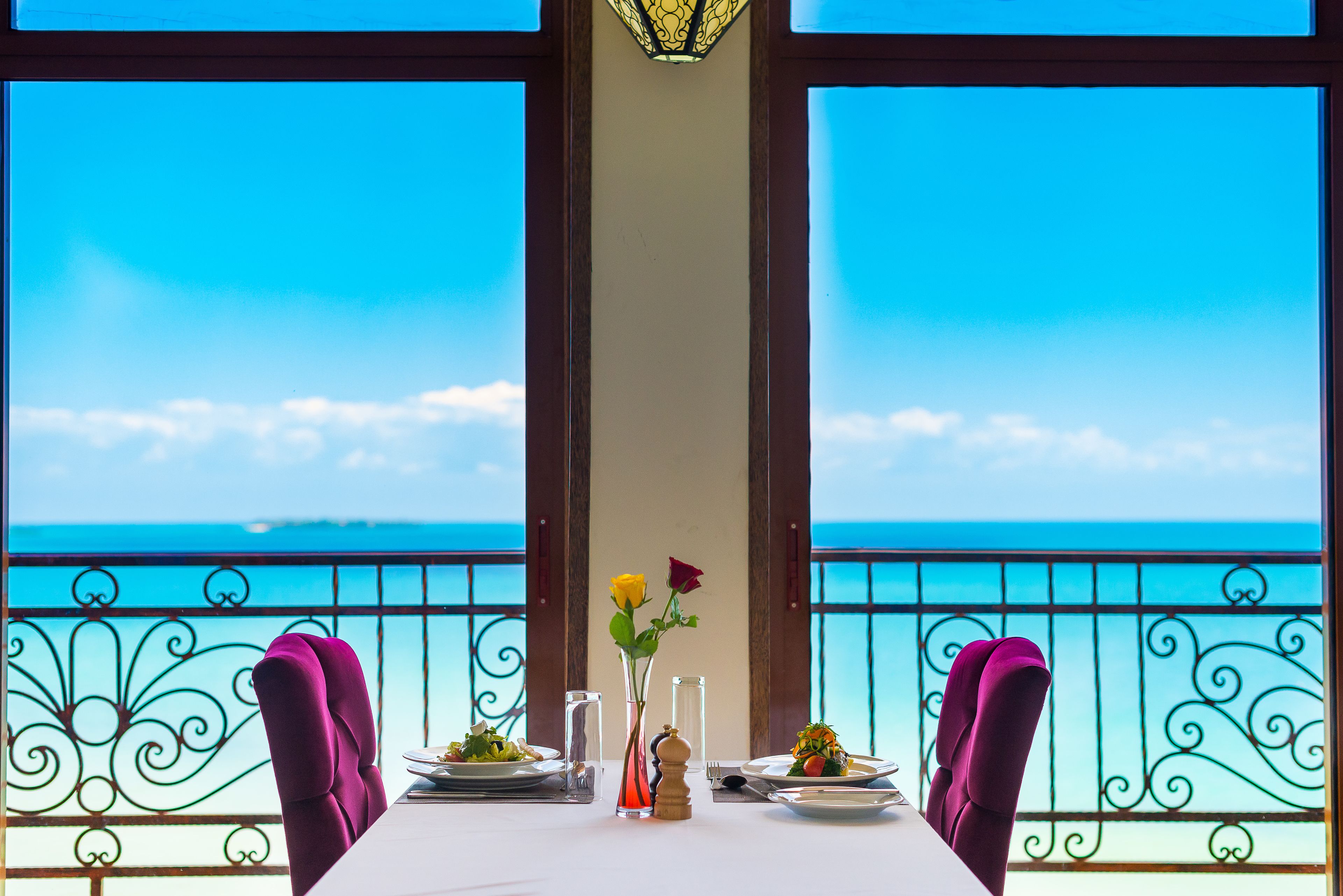 A table set for two with a view of the sea, a vase with flowers, and a salt shaker.