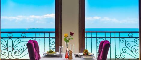 A table set for two with a view of the sea, a vase with flowers, and a salt shaker.