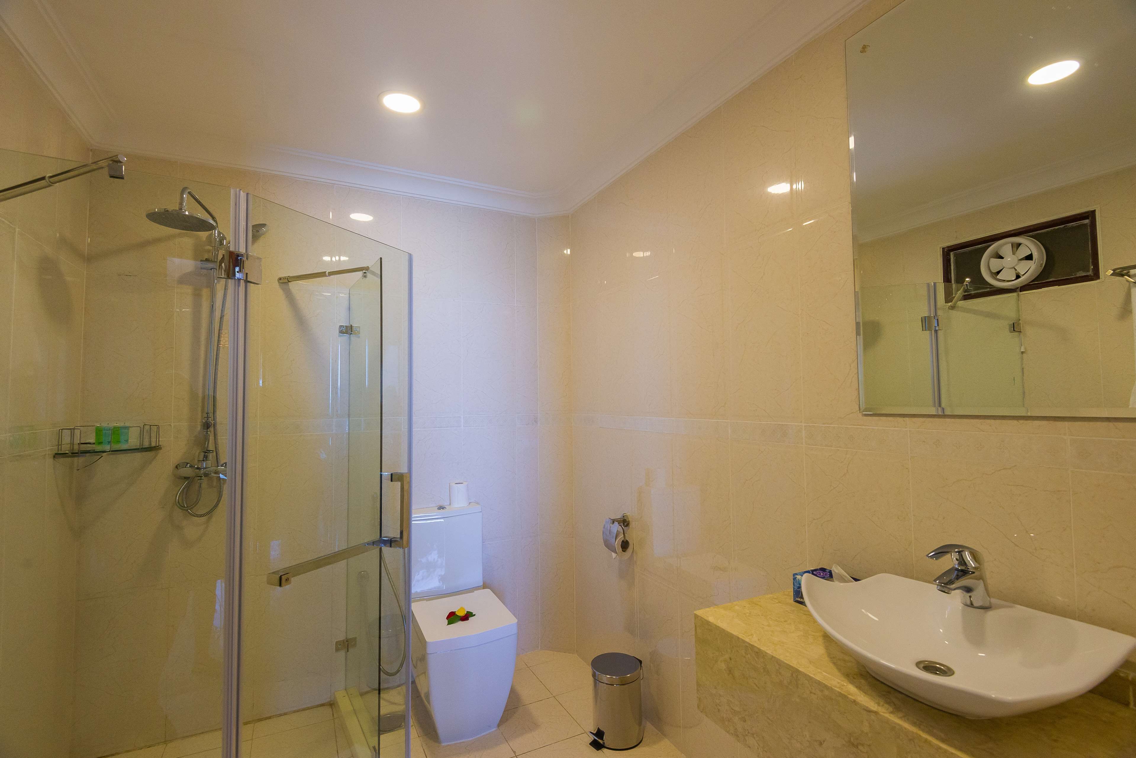 A bathroom with a glass-enclosed shower, a white toilet, a sink with a mirror above it, and a trash can.