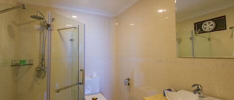 A bathroom with a glass-enclosed shower, a white toilet, a sink with a mirror above it, and a trash can.