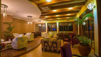 A hotel lobby with a curved ceiling, patterned sofas, a central coffee table, and potted plants.