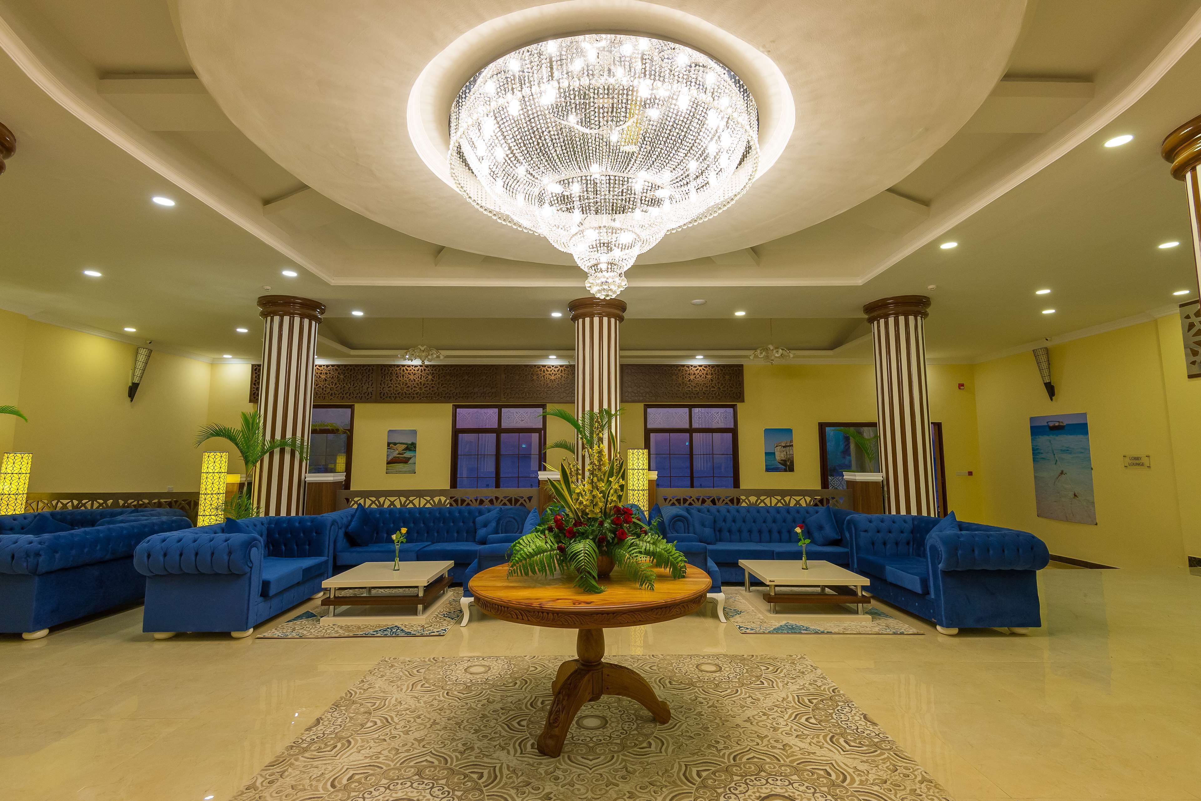 A lobby with blue sofas, a central round table with a floral arrangement, and a large chandelier.
