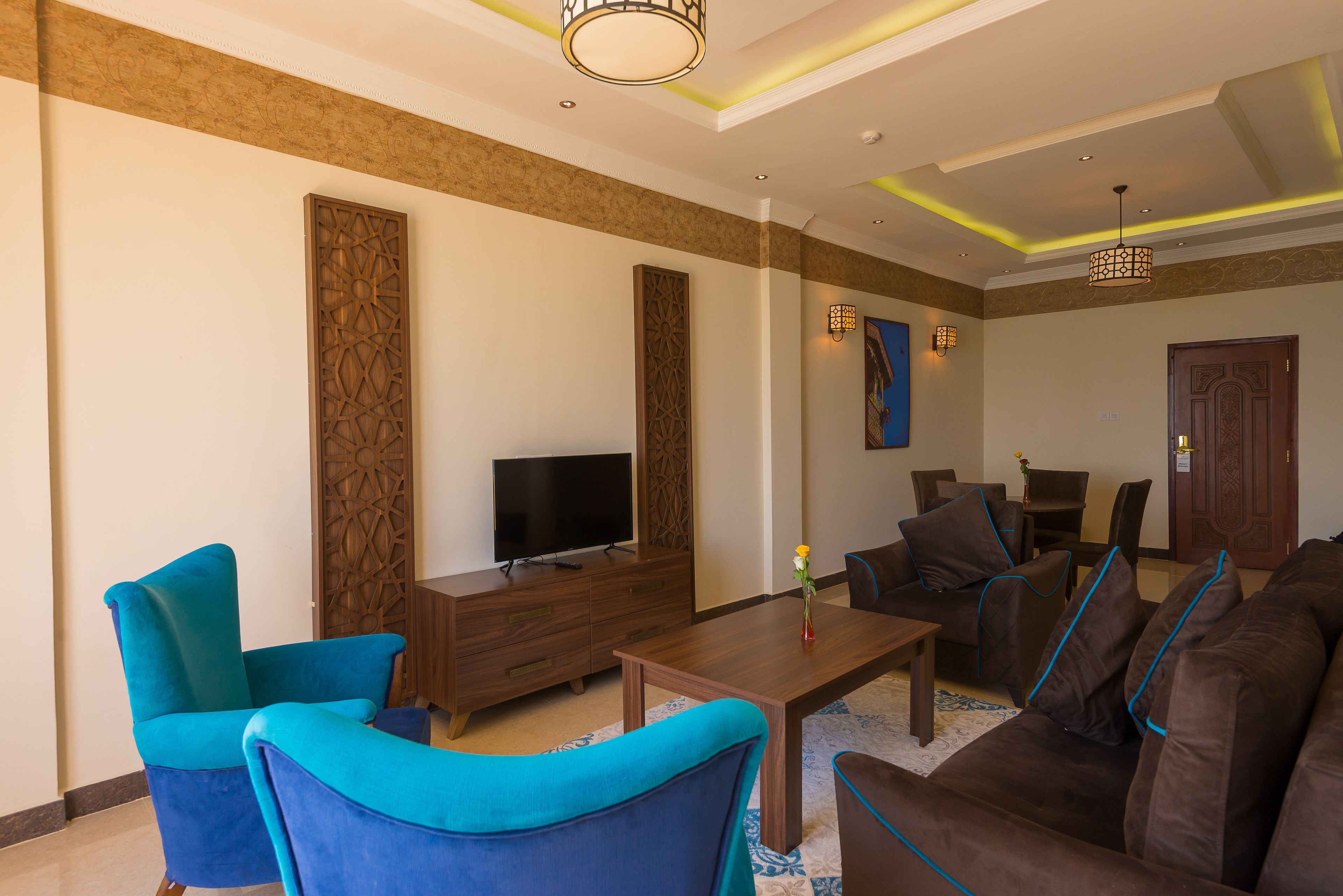 A modern living room with a flat-screen TV, blue armchairs, a brown sofa, and a wooden coffee table.