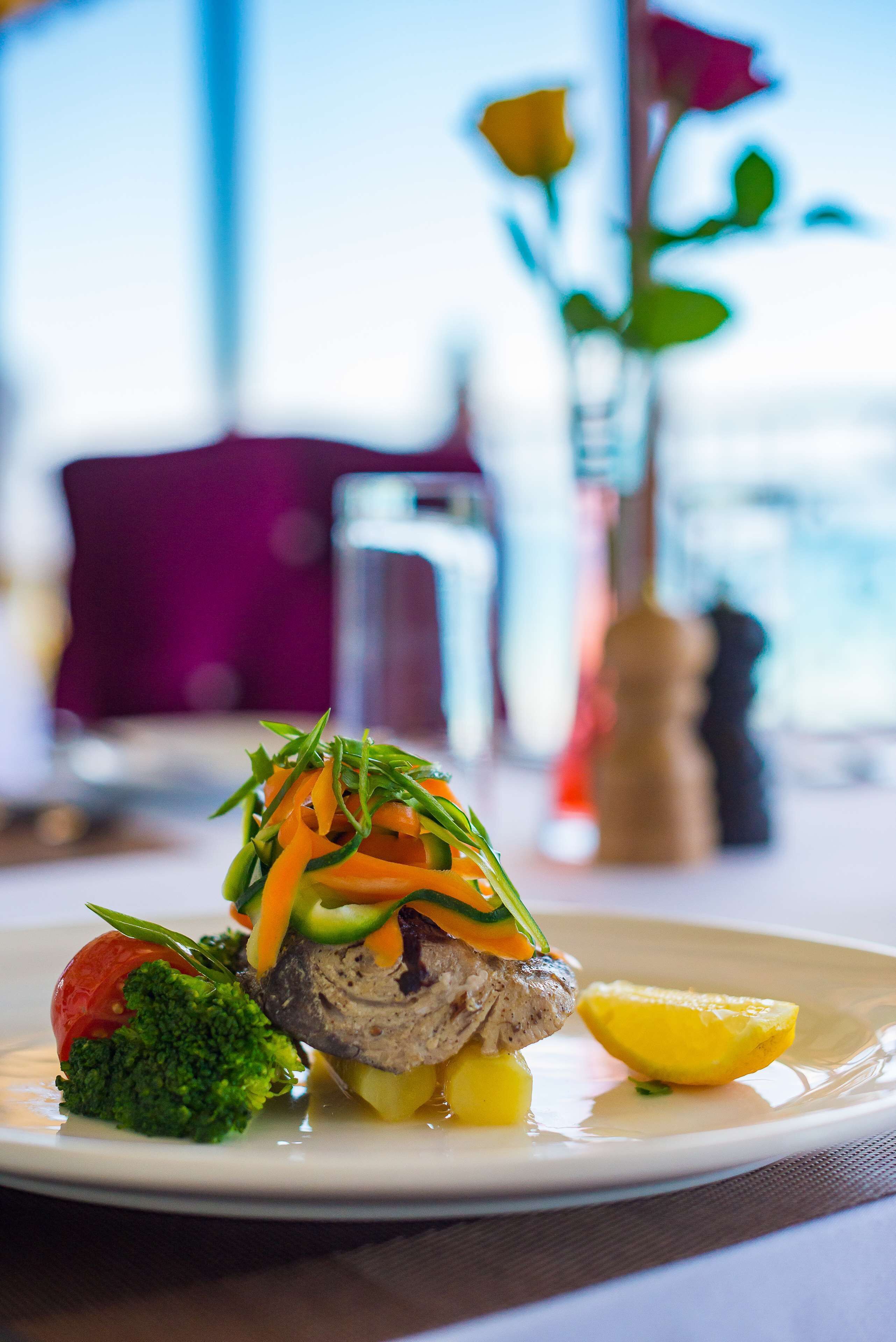 A plate of food with a piece of meat, vegetables, and a lemon wedge.