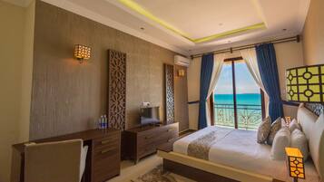 A hotel room with a bed, a desk, a chair, a TV, and a view of the ocean.