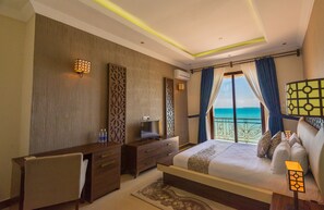 Une chambre d’hôtel avec un lit, un bureau, une chaise, une télévision et une vue sur l’océan.