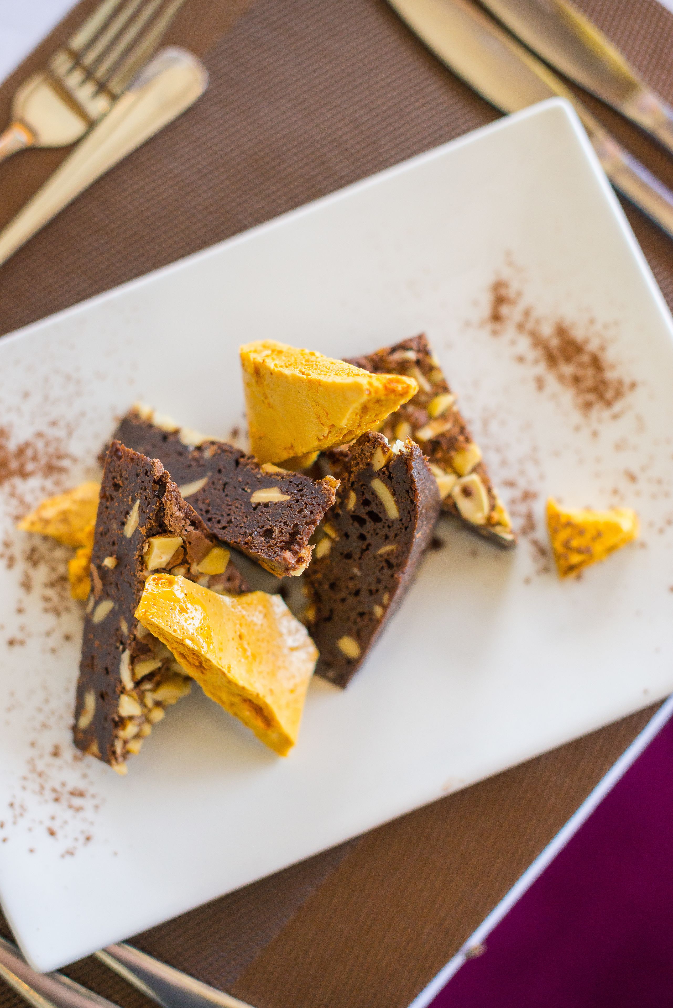 Un plato blanco con porciones de chocolate y color amarillo, posiblemente un postre, sobre una mesa con un mantel individual marrón.