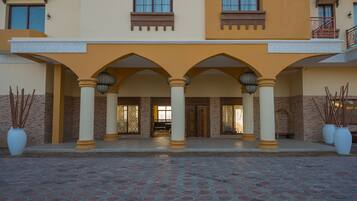 A hotel entrance with a covered walkway, columns, and potted plants.