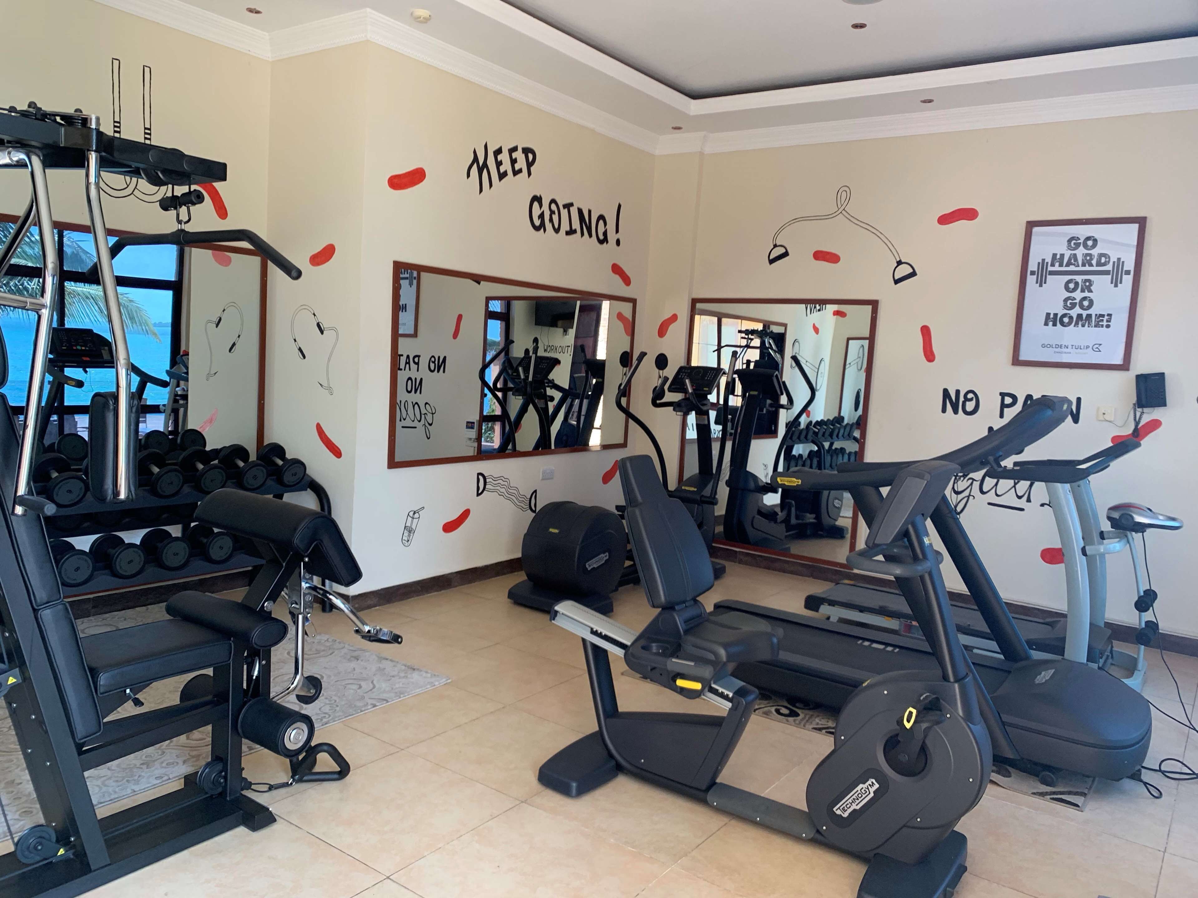 Een sportschool met fitnessapparatuur, motiverende muurdecoratie en een grote spiegel.