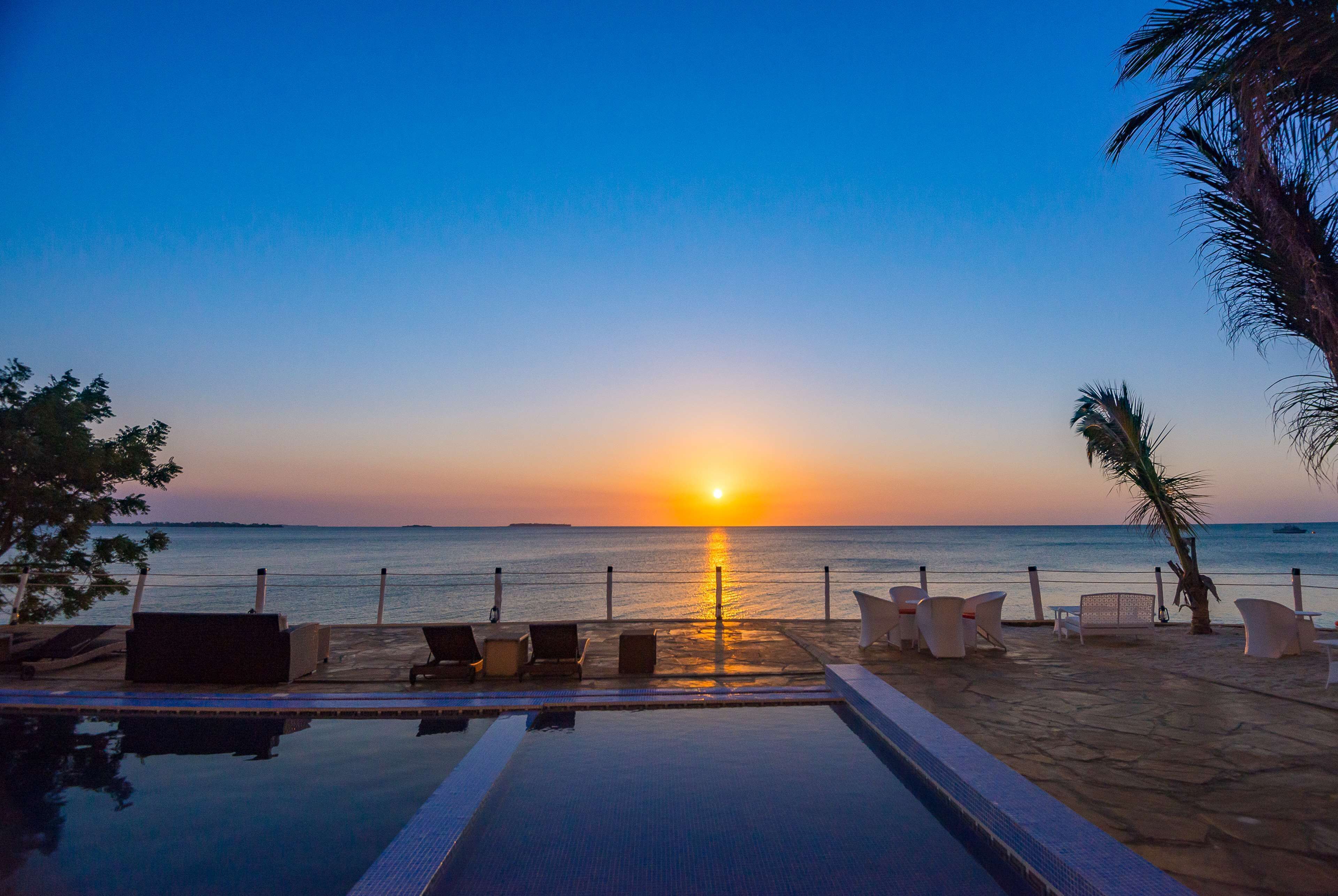A poolside view with lounge chairs and a sunset over the ocean.