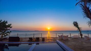 A poolside view with lounge chairs and a sunset over the ocean.