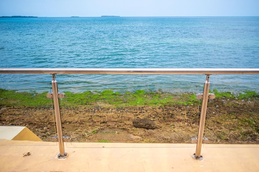 Vista di una spiaggia con una ringhiera metallica in primo piano e l'oceano sullo sfondo.
