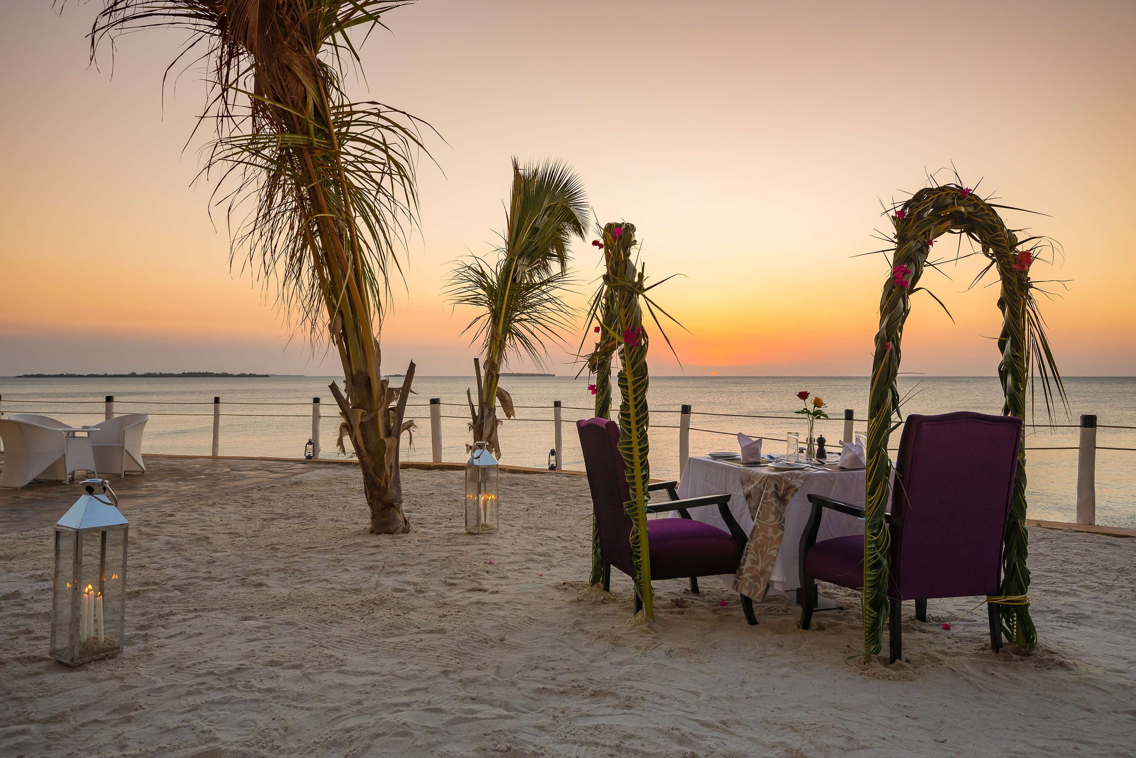 Ein Essbereich am Strand mit Tisch und Stühlen, einer Laterne und einem Zierbogen.