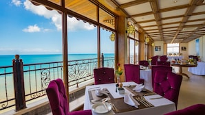 Un restaurante con mesas preparadas para comer, un balcón con vista al mar y un techo de madera.