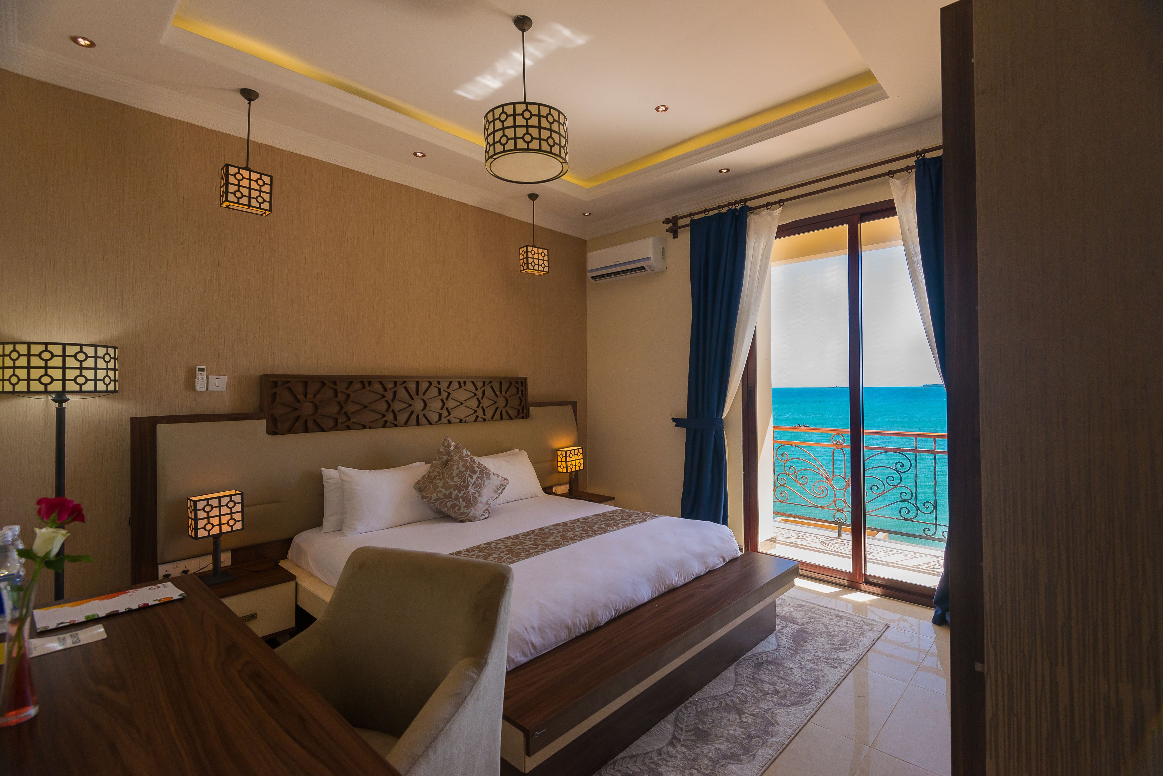 A hotel room with a bed, bedside lamps, a desk, and a view of the ocean.