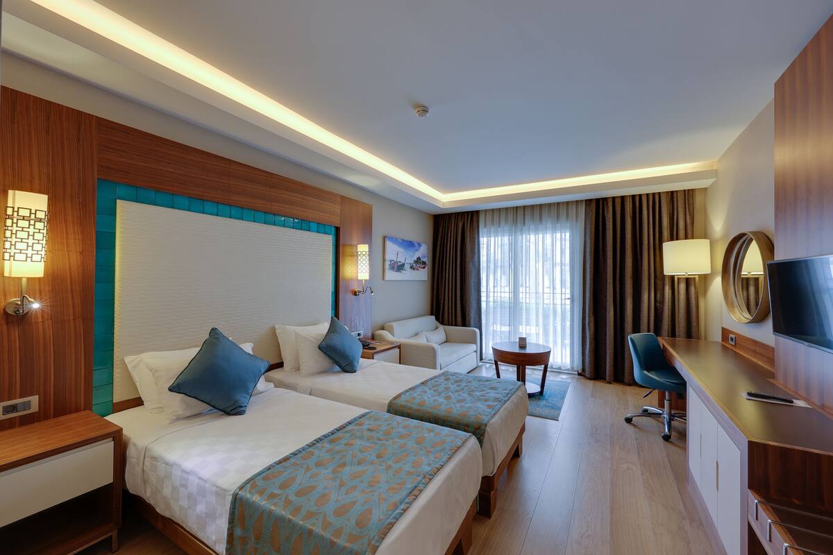 A hotel room with two beds, a desk, a chair, a TV, and a window with curtains.