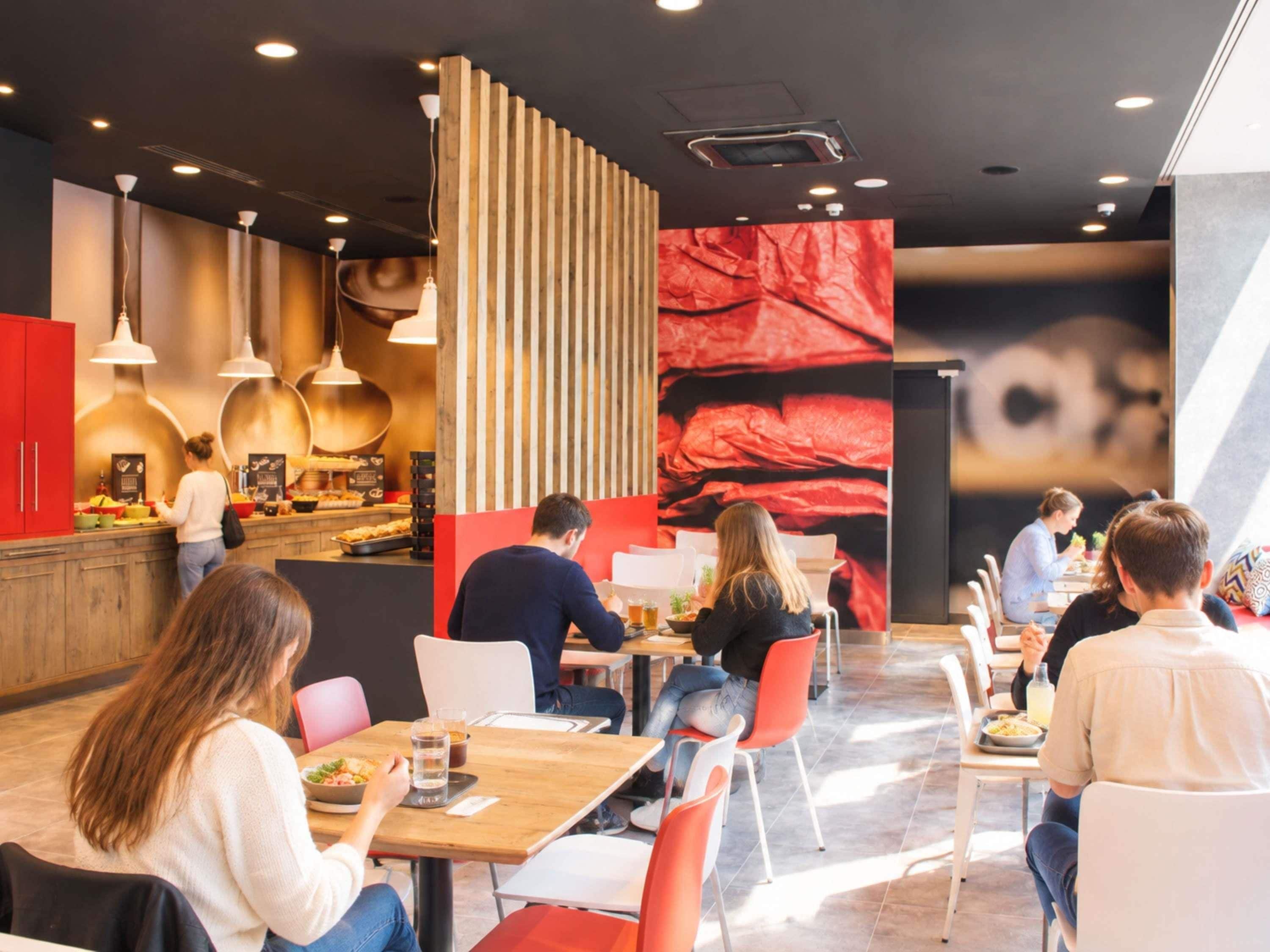 A modern restaurant interior with a counter, seating area, and a large red mural.