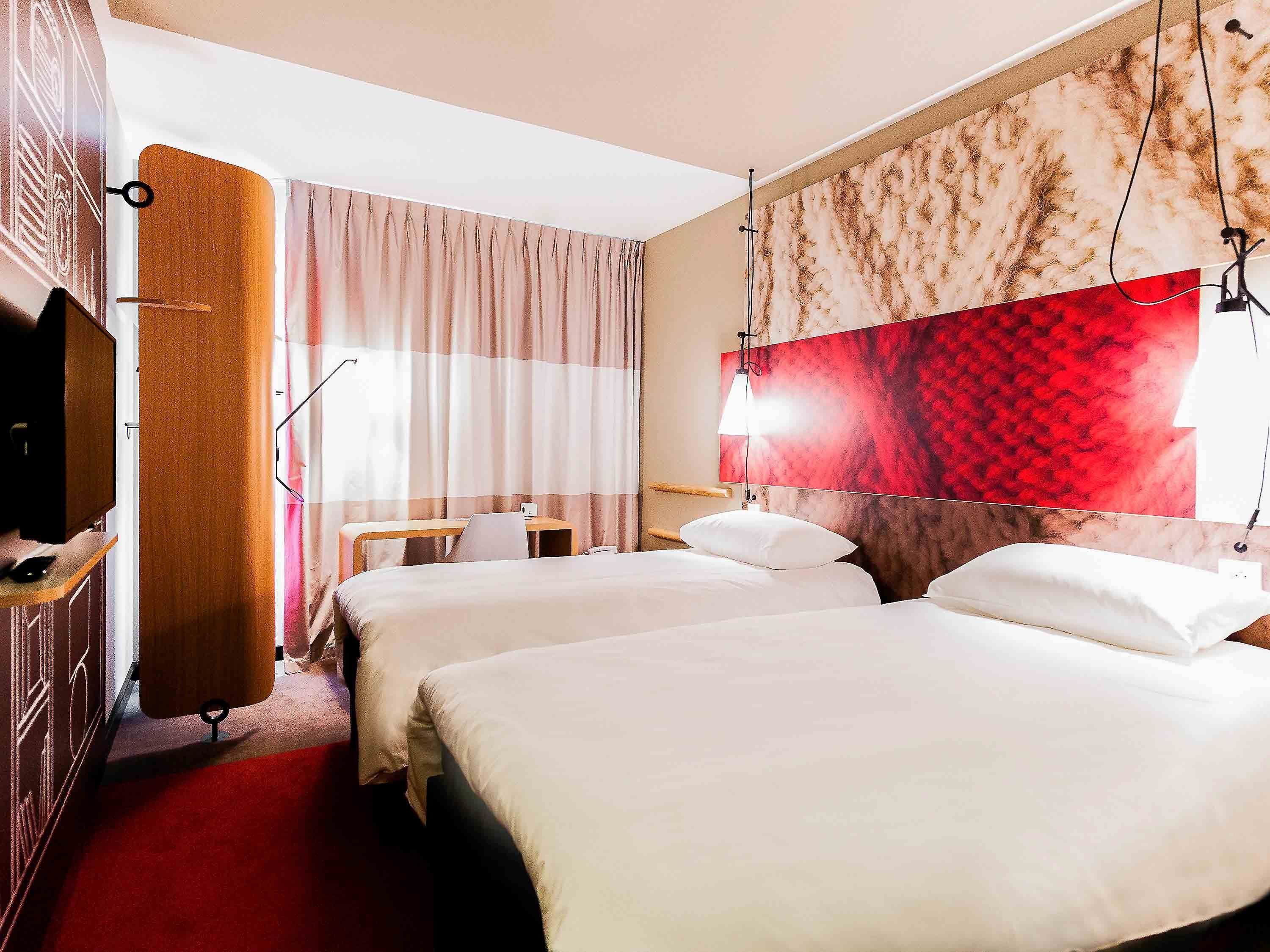 Habitación de hotel con dos camas, un escritorio, un televisor y un mural grande de color rojo y beige.