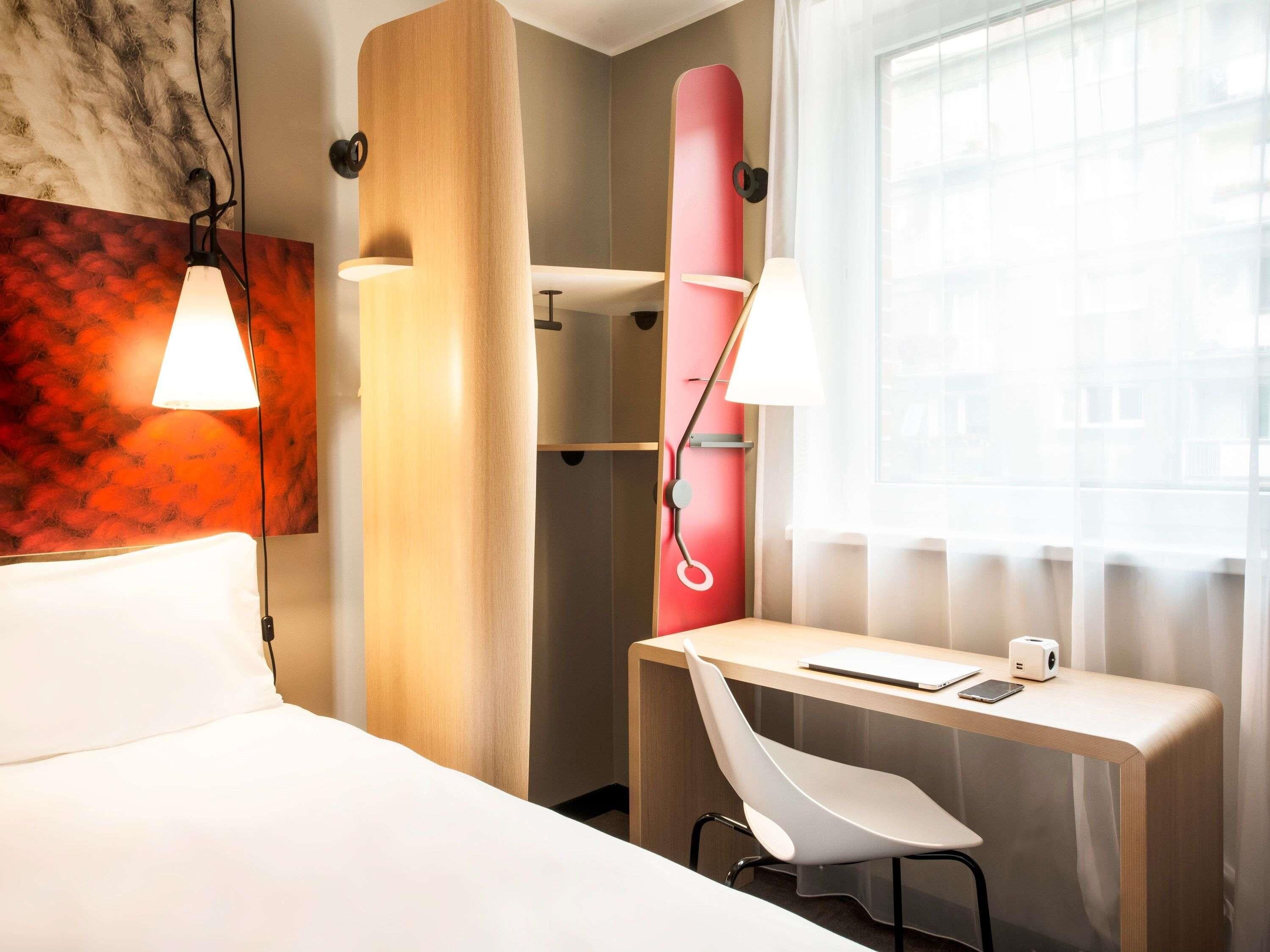 A hotel room with a bed, desk, chair, and a window with curtains.