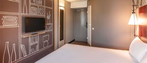 A hotel room with a large bed, a flat-screen TV mounted on the wall, and a bedside lamp.