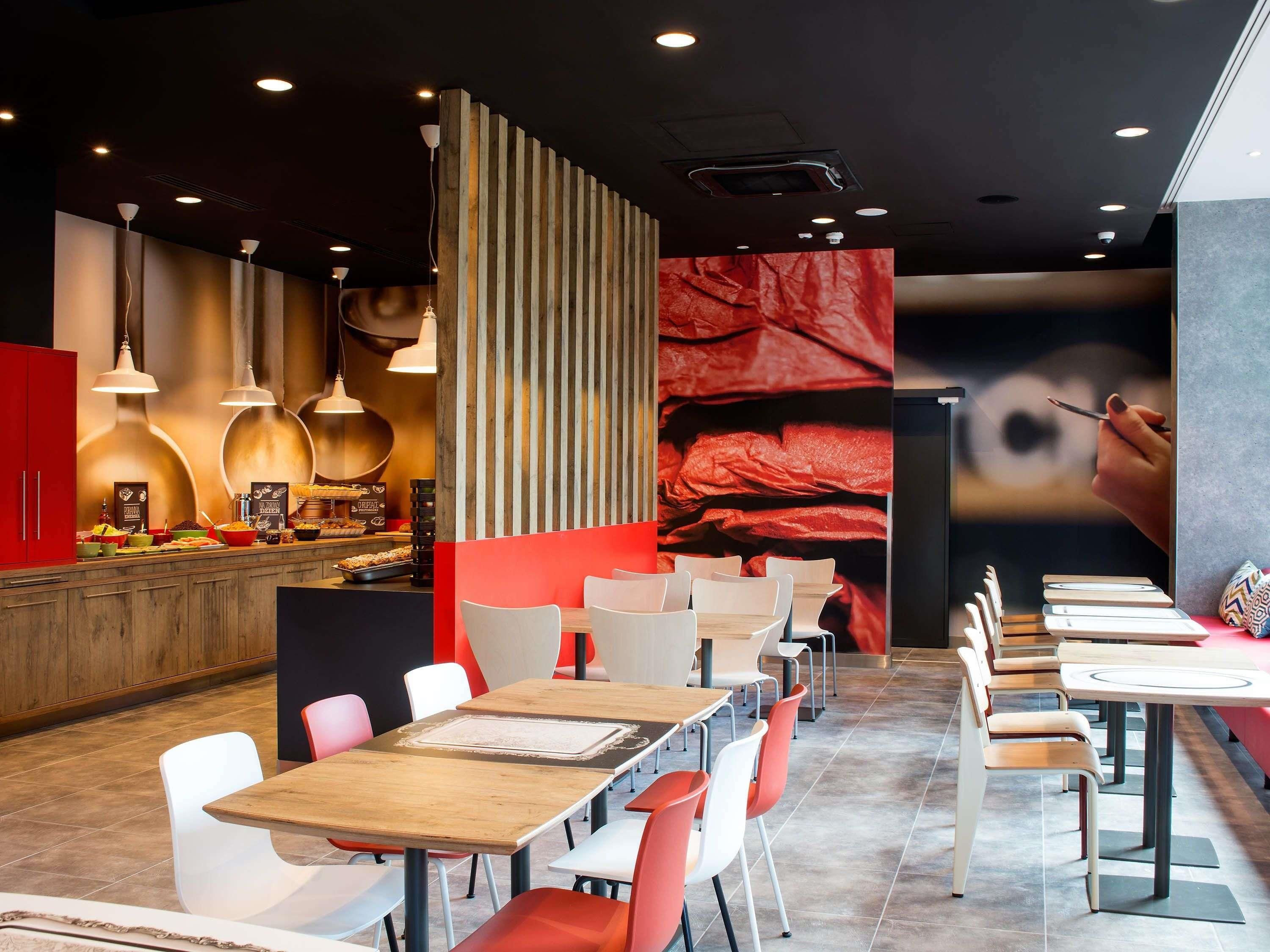 A modern restaurant interior with wooden tables and chairs, a counter with food items, and pendant lighting.