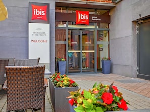 An exterior of a hotel with wicker furniture and potted plants.
